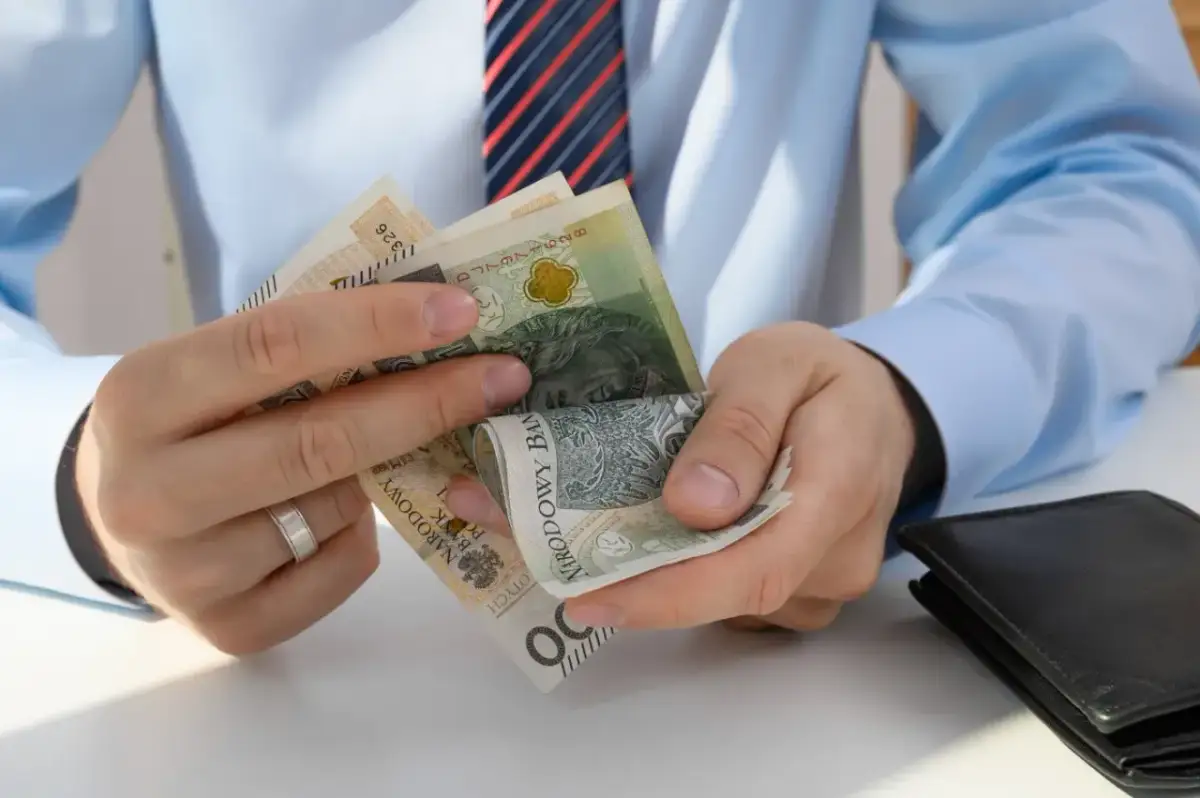 Dłonie liczące polskie banknoty, obok czarny portfel.