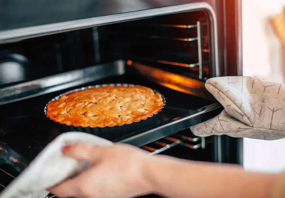 Ręka w rękawicy wyjmuje z piekarnika z termoobiegiem złocisty placek.