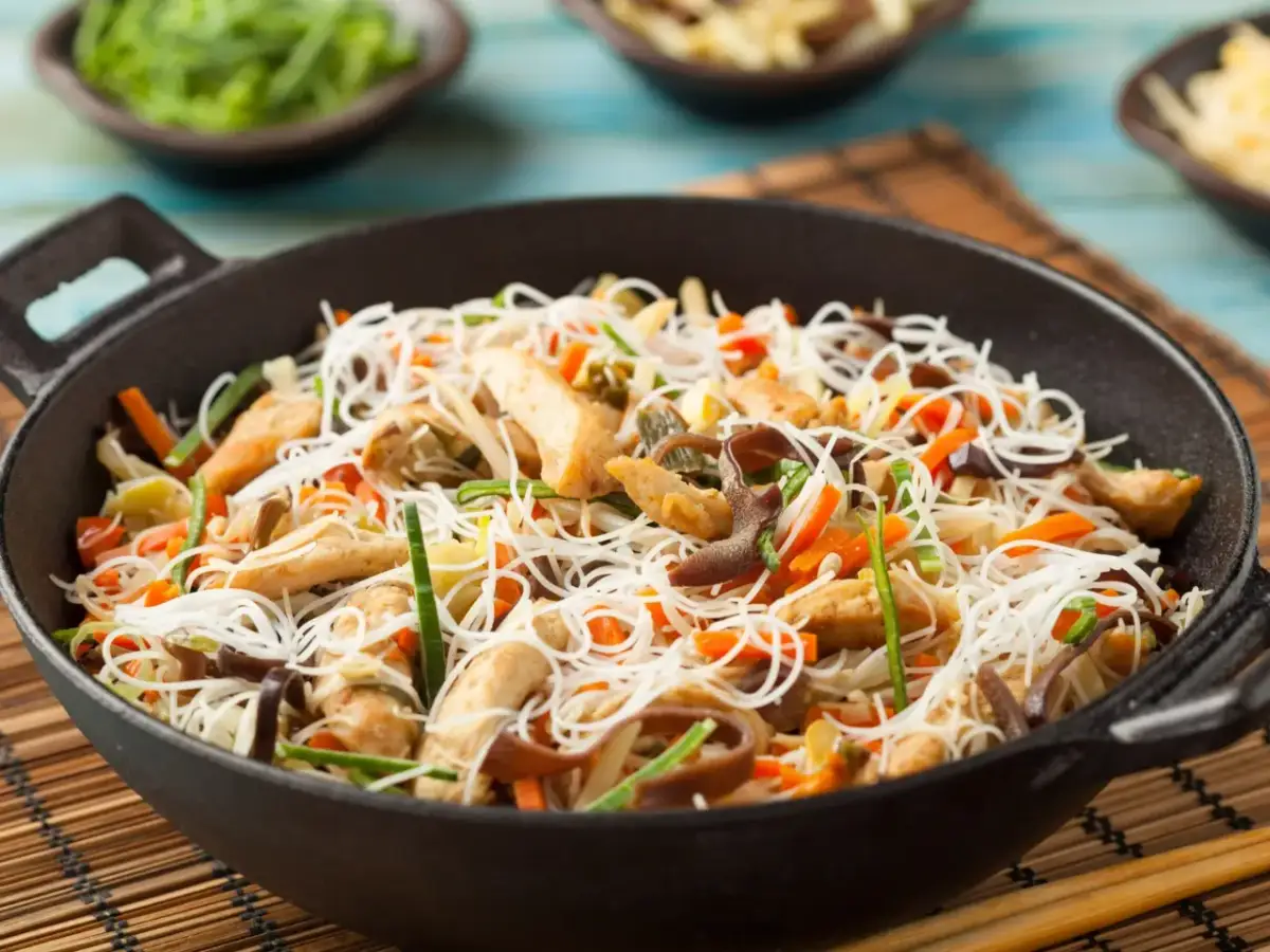 Pyszna sałatka z makaronem ryżowym i kurczakiem, pełna warzyw i grzybów mun, podana w woku.