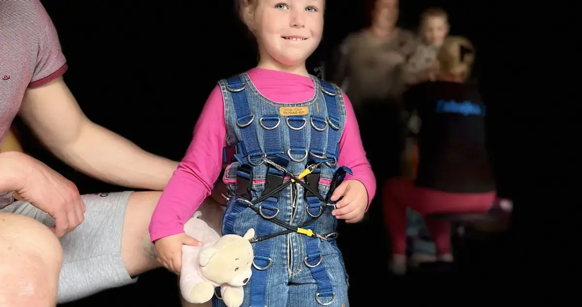 Uśmiechnięta dziewczynka w niebieskim kombinezonie Dunag, trzymająca misia. Gdzie kupić taki kombinezon?