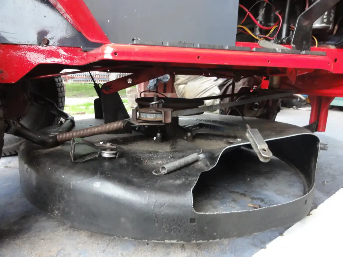 Podczas naprawy traktorka, widać mechanizm kosiska z pasem napędowym i sprężyną.