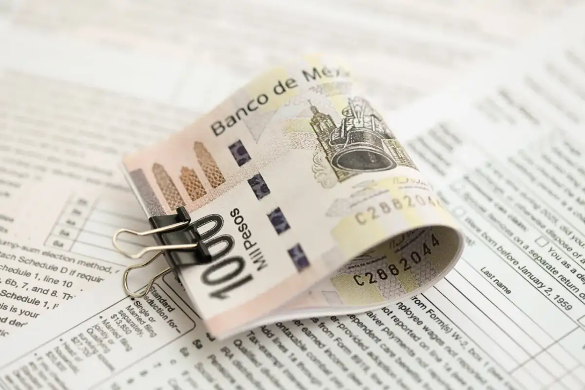 Złożony banknot 100 pesos, przytrzymany spinaczem, leży na dokumentach podatkowych. To pokazuje, co to jest lokata bankowa – sposób na bezpieczne przechowywanie pieniędzy.