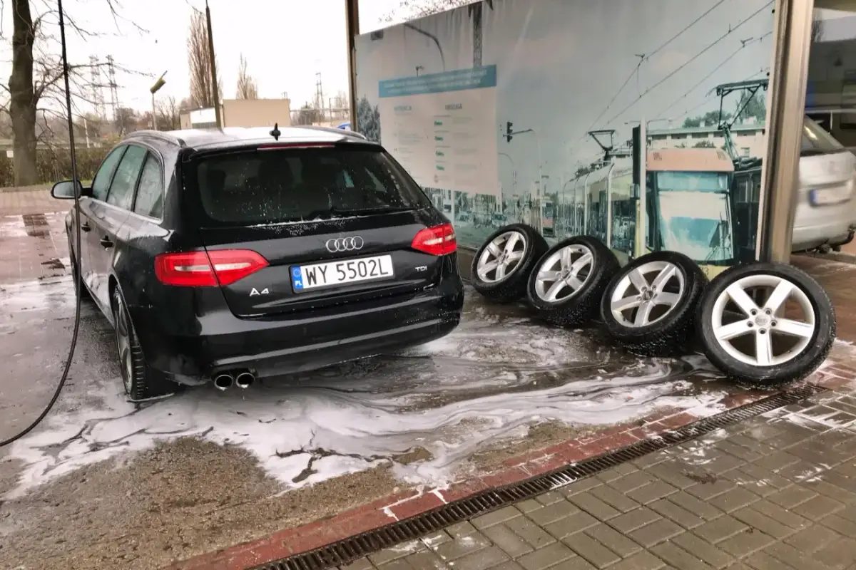 Czarny Audi na myjni bezdotykowej, obok cztery koła. Poznaj myjnia bezdotykowa triki, by Twój samochód lśnił!