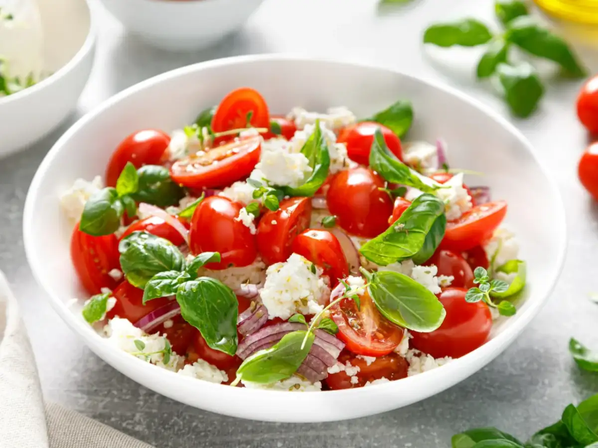 Sałatka z pomidorków koktajlowych, sera feta i bazylii. Idealna na lato, pokazuje, jak pokroić pomidora do sałatki.