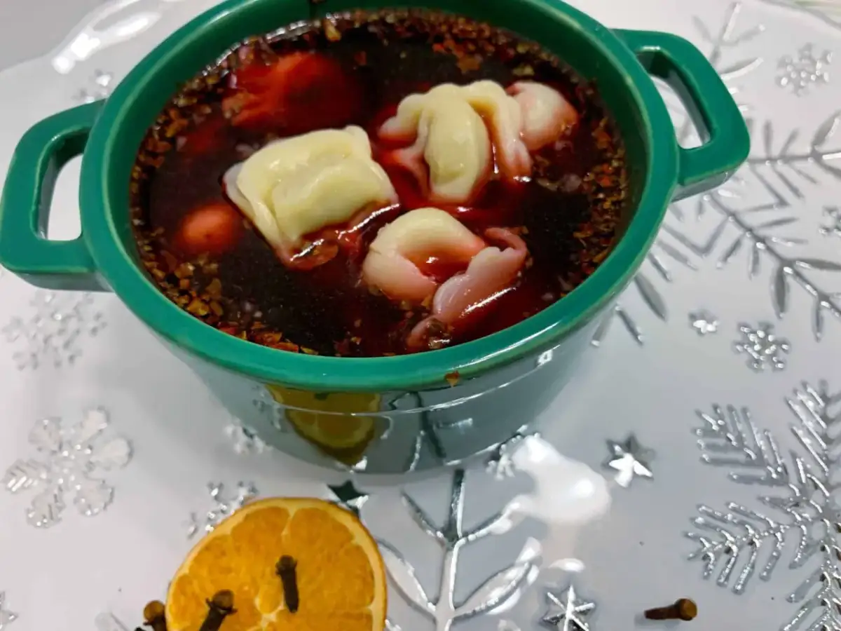 Aromaticzny barszcz z uszkami w zielonej miseczce, ozdobiony suszoną pomarańczą i goździkami.