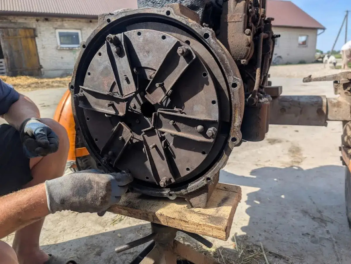 Mechanik w rękawiczkach reguluje mechanizm sprzęgła, przygotowując traktor do pracy.