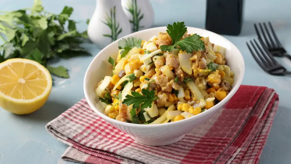 Pyszna sałatka z makreli z jajkiem, kukurydzą i natką pietruszki, podana w białej misce na czerwono-białej serwetce.