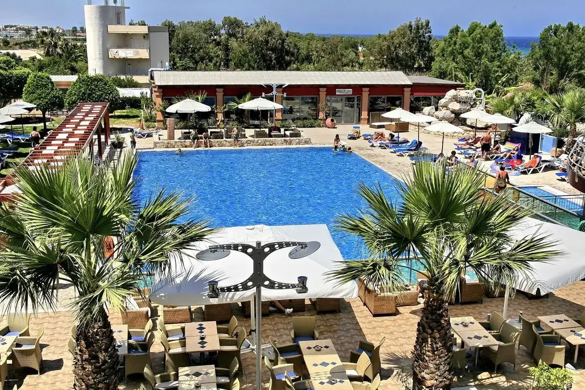 Basen z turkusową wodą, leżaki, palmy i stoliki w greckim kurorcie.