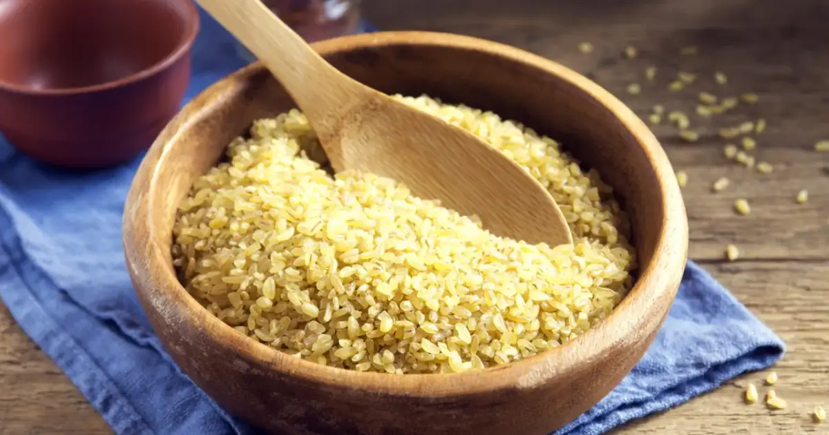 Drewniana miska pełna kaszy bulgur z drewnianą łyżką.
