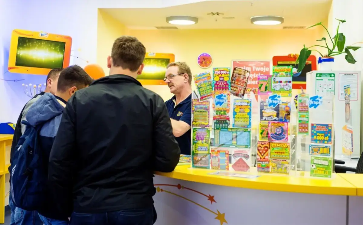 Mężczyźni stoją przy ladzie, na której widać wiele zdrapek Lotto. Czy na Orlenie są zdrapki Lotto? Tak, jak widać na zdjęciu.