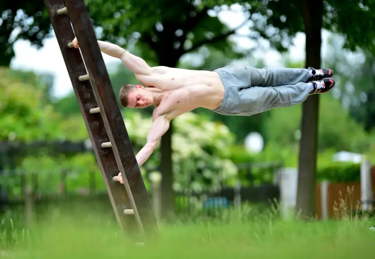 Mężczyzna wykonuje figurę "human flag" na drabinie. To przykład tego, kalistenika co to za dyscyplina – siła i kontrola ciała.