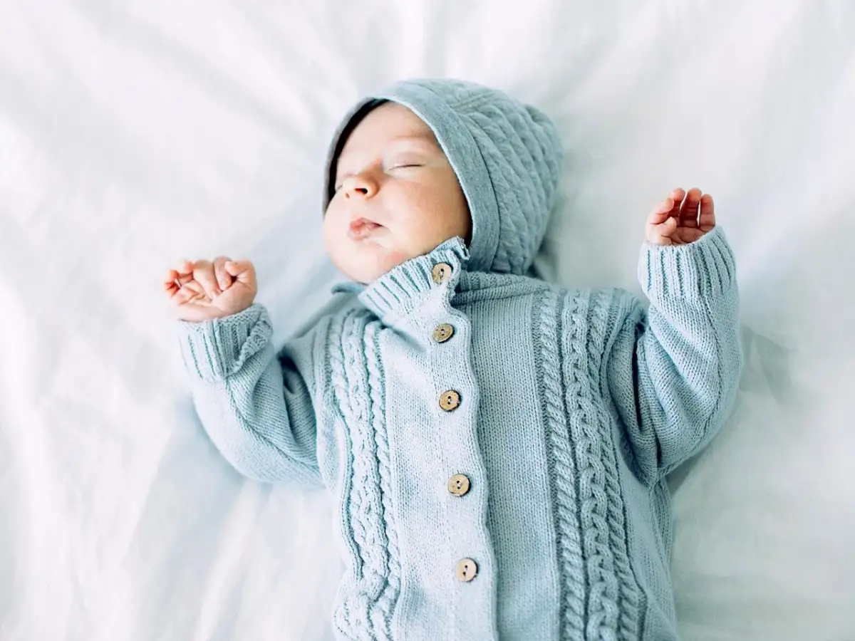 Śpiący maluszek w błękitnym, dzierganym kombinezonie z kapturem. Idealny przykład, jak zrobić kombinezon na drutach dla niemowlaka.