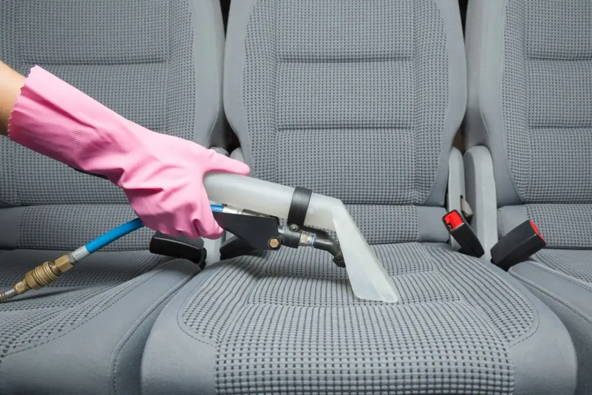 Rękawica w różowej rękawiczce używa odkurzacza ekstrakcyjnego, pokazując, jak wyczyścić tapicerkę w aucie na sucho.