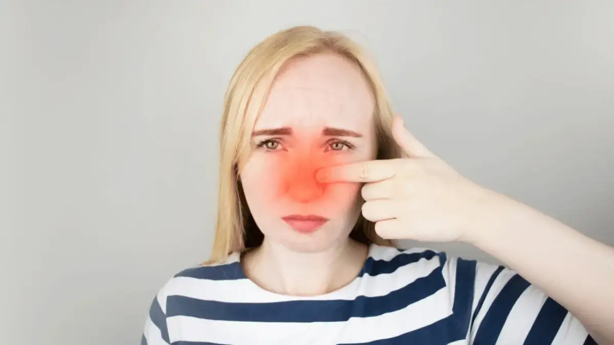 Kobieta z zaczerwienionym nosem, wskazująca palcem na ból. Szuka informacji, jak leczyć zatoki.