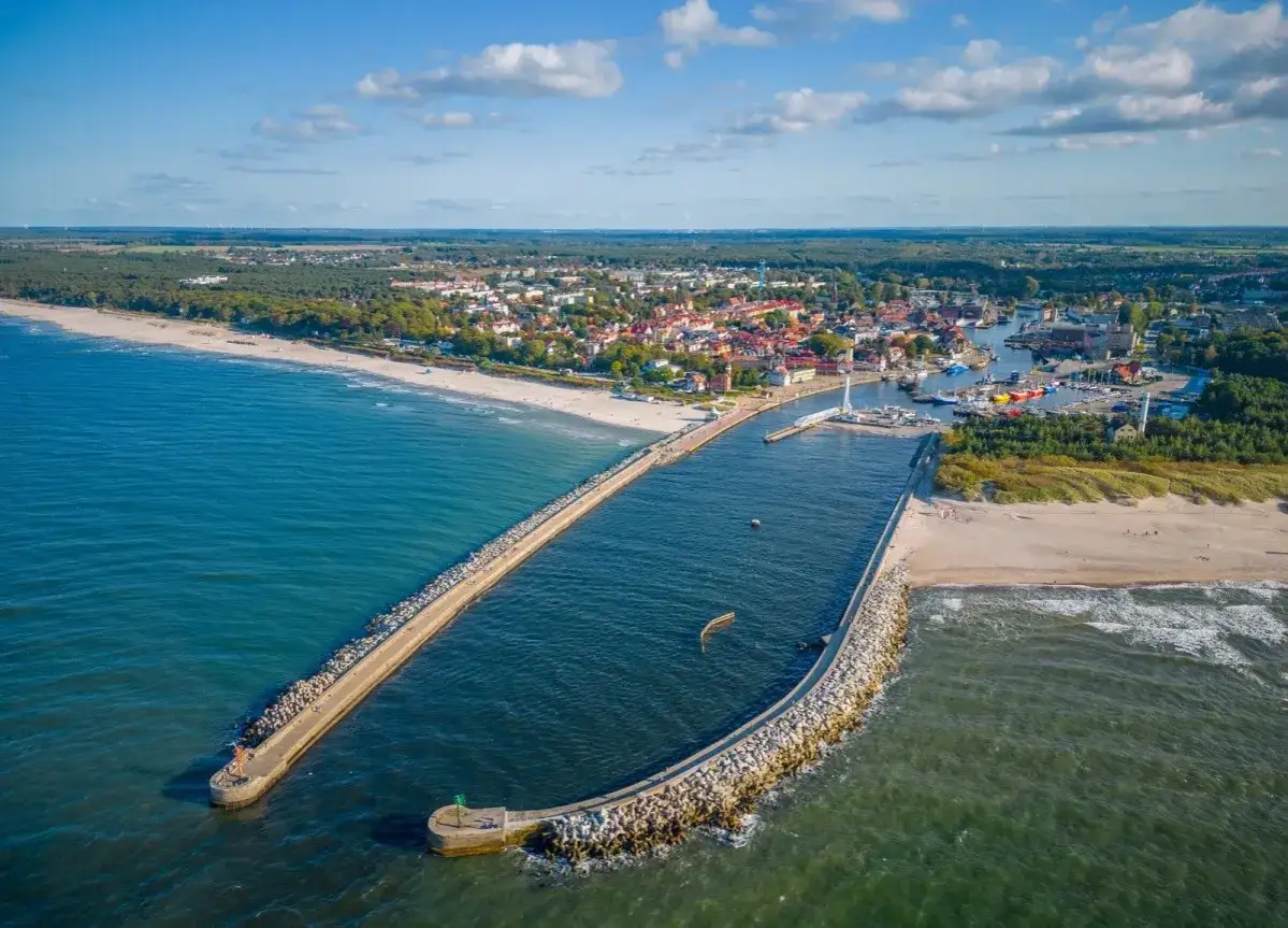 Widok z lotu ptaka na port w Ustce z falochronami, plażą i miastem w tle.