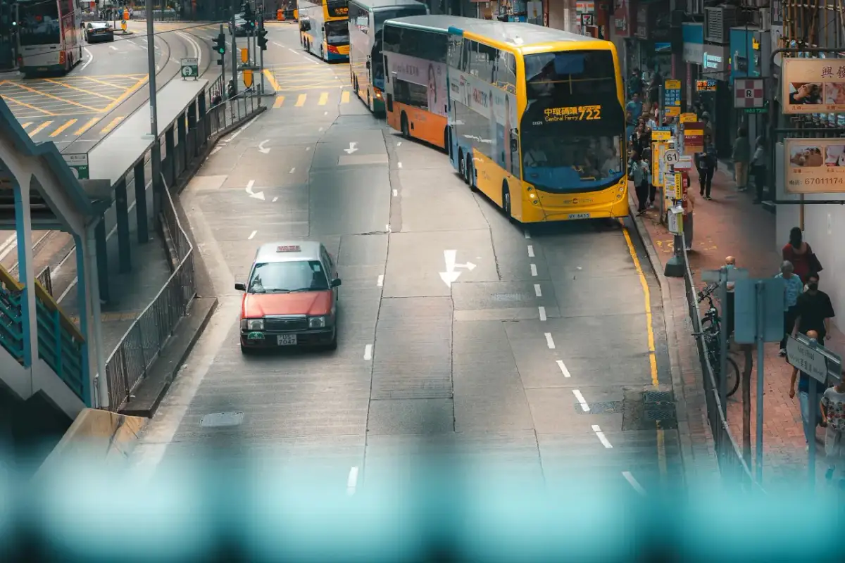 Czerwona taksówka i żółty autobus miejski poruszają się po ruchliwej ulicy. To typowe auto do miasta, które ułatwia poruszanie się po zatłoczonych ulicach.