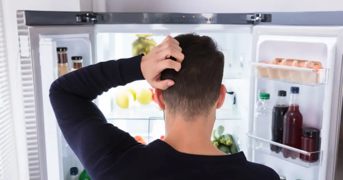 Mężczyzna drapie się po głowie przed otwartą lodówką, zastanawiając się, jak obniżyć poziom greliny i co zjeść.