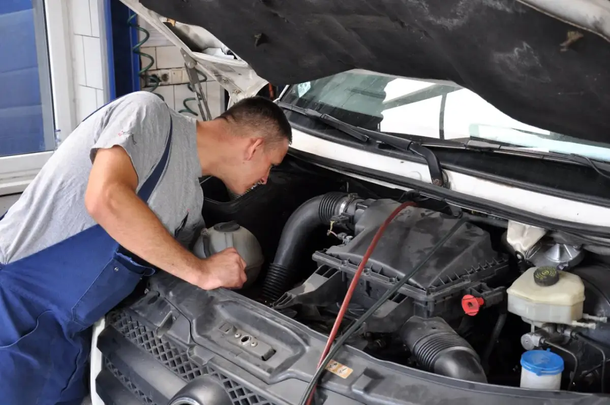 Mechanik pochyla się nad silnikiem, przygotowując się do wymiany świec żarowych.