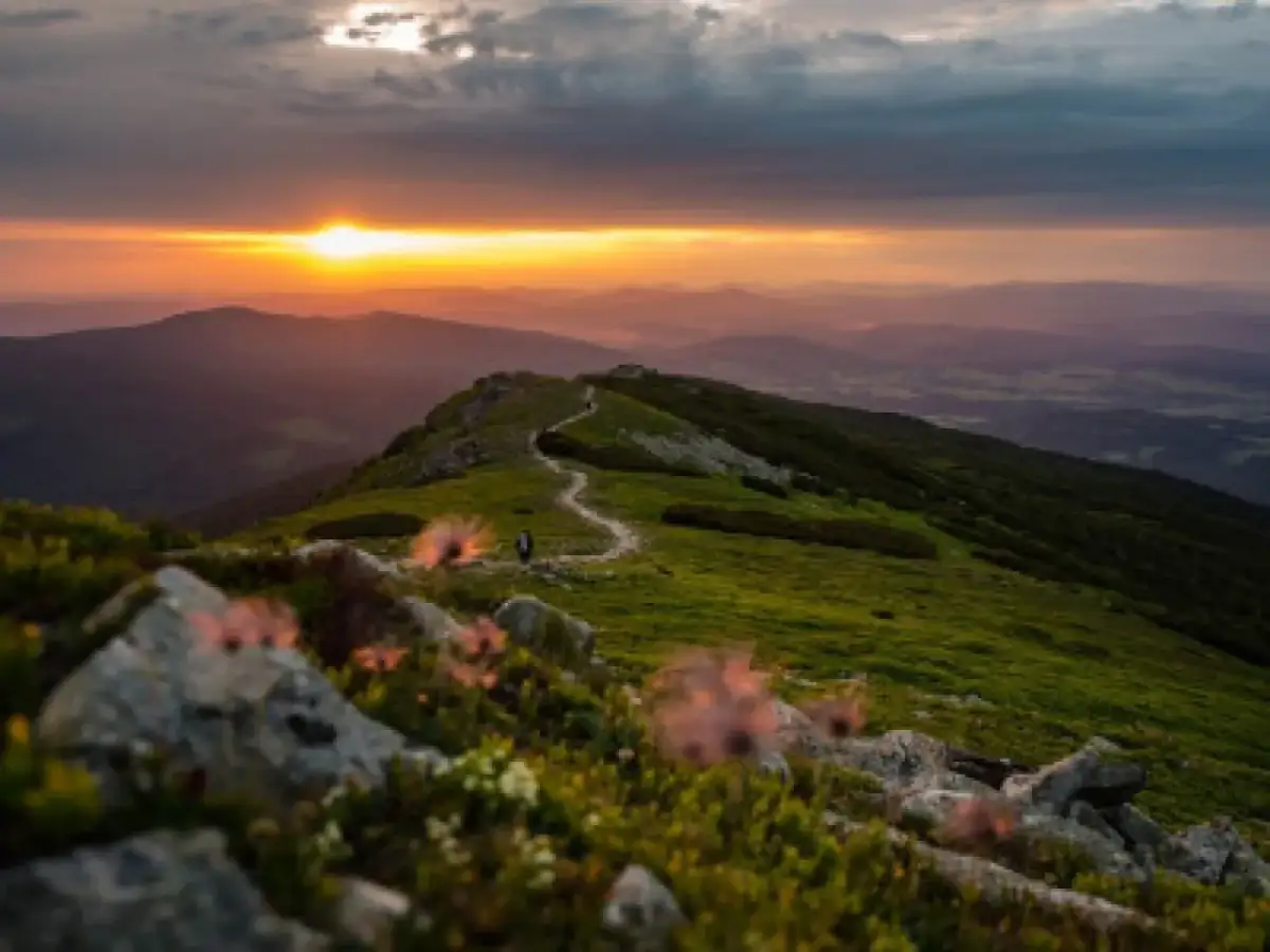 Zachód słońca nad pasmem górskim z krętą ścieżką i pojedynczym turystą.