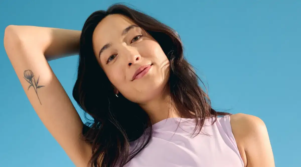 Kobieta z delikatnym tatuażem kwiatu na ramieniu. Czy tatuaż można smarować kremem Nivea? Zapytaj eksperta.