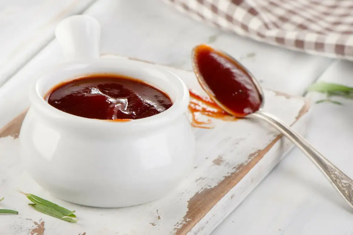 Pyszny, gęsty sos barbecue w białej sosjerce i na łyżce. Idealny przykład, jak zrobić sosy, które wzbogacą każde danie.