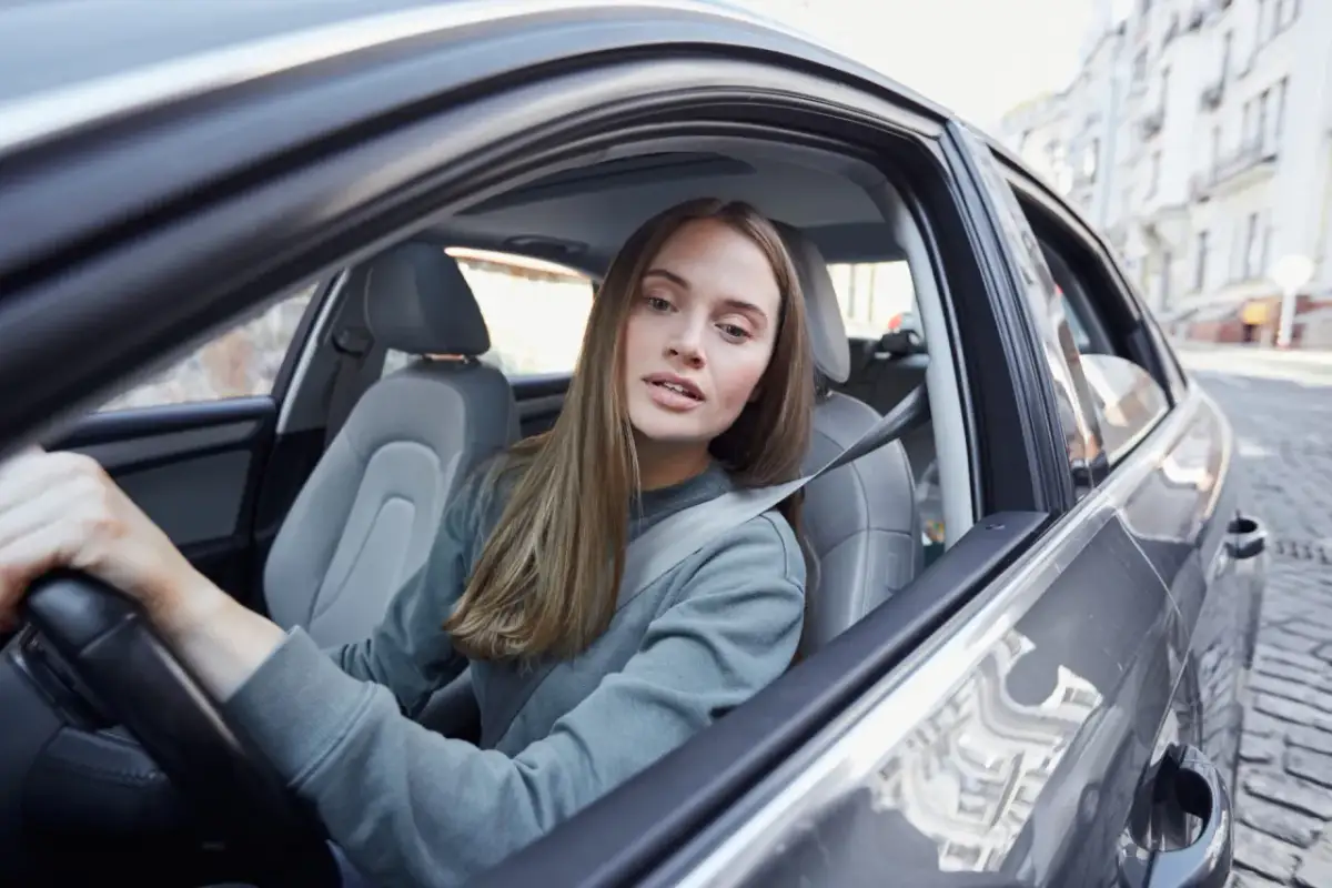Młoda kobieta, współwłaściciel samochodu poniżej 25 roku życia, prowadzi auto po brukowanej ulicy.