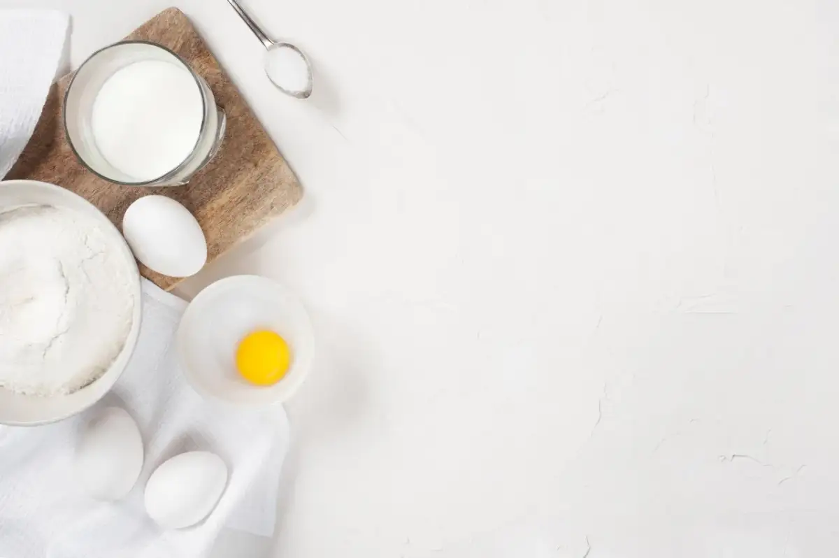 Mąka, jajka, mleko i łyżeczka cukru na białym tle.