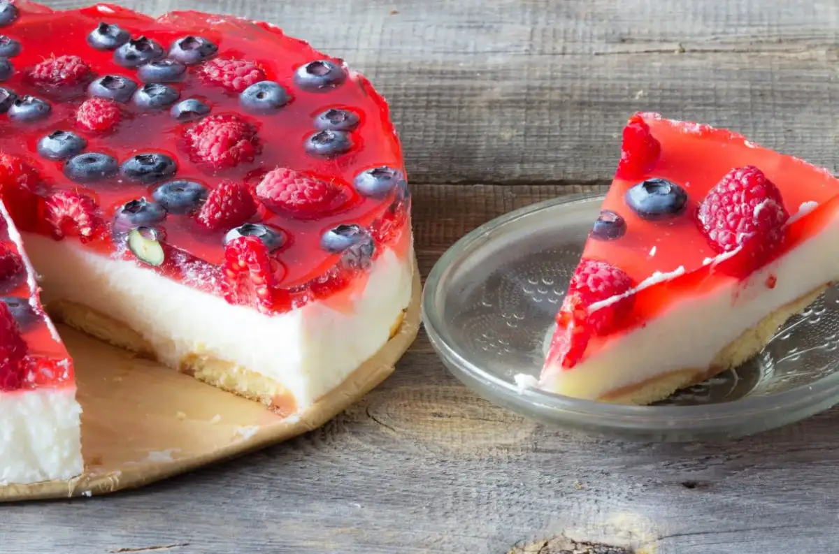 Pyszne ciasto z galaretką i owocami leśnymi, z kawałkiem na talerzyku.