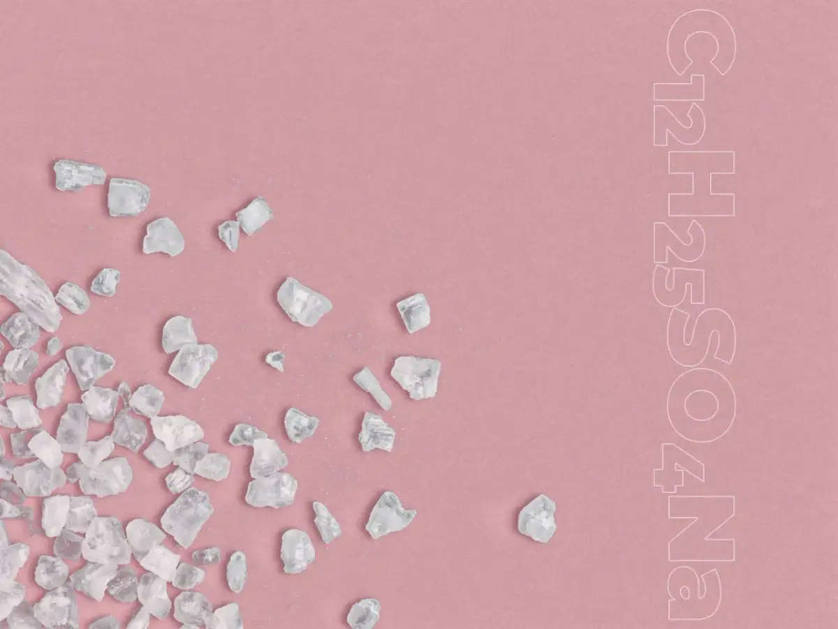 Kryształki disodium laureth sulfosuccinate rozsypane na różowym tle.