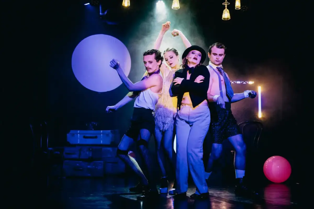 Czterech artystów na scenie, w teatralnych strojach, tworzy atmosferę o nierządne królestwo i zginienia bliskie.