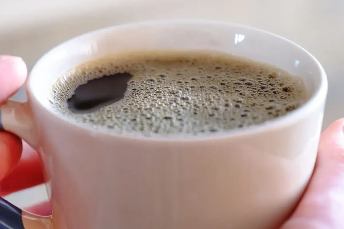 Gorąca kawa w kubku, która pobudza, bo tak działa kofeina. Piana na powierzchni świadczy o świeżości napoju.