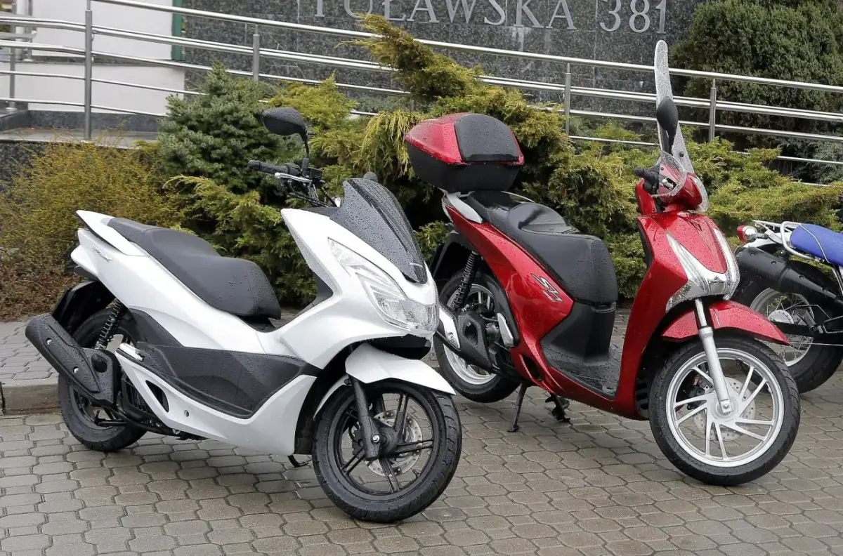 Dwa skutery, biały i czerwony, stoją na mokrym chodniku. Pytanie: co ile wymiana oleju w skuterze 50?