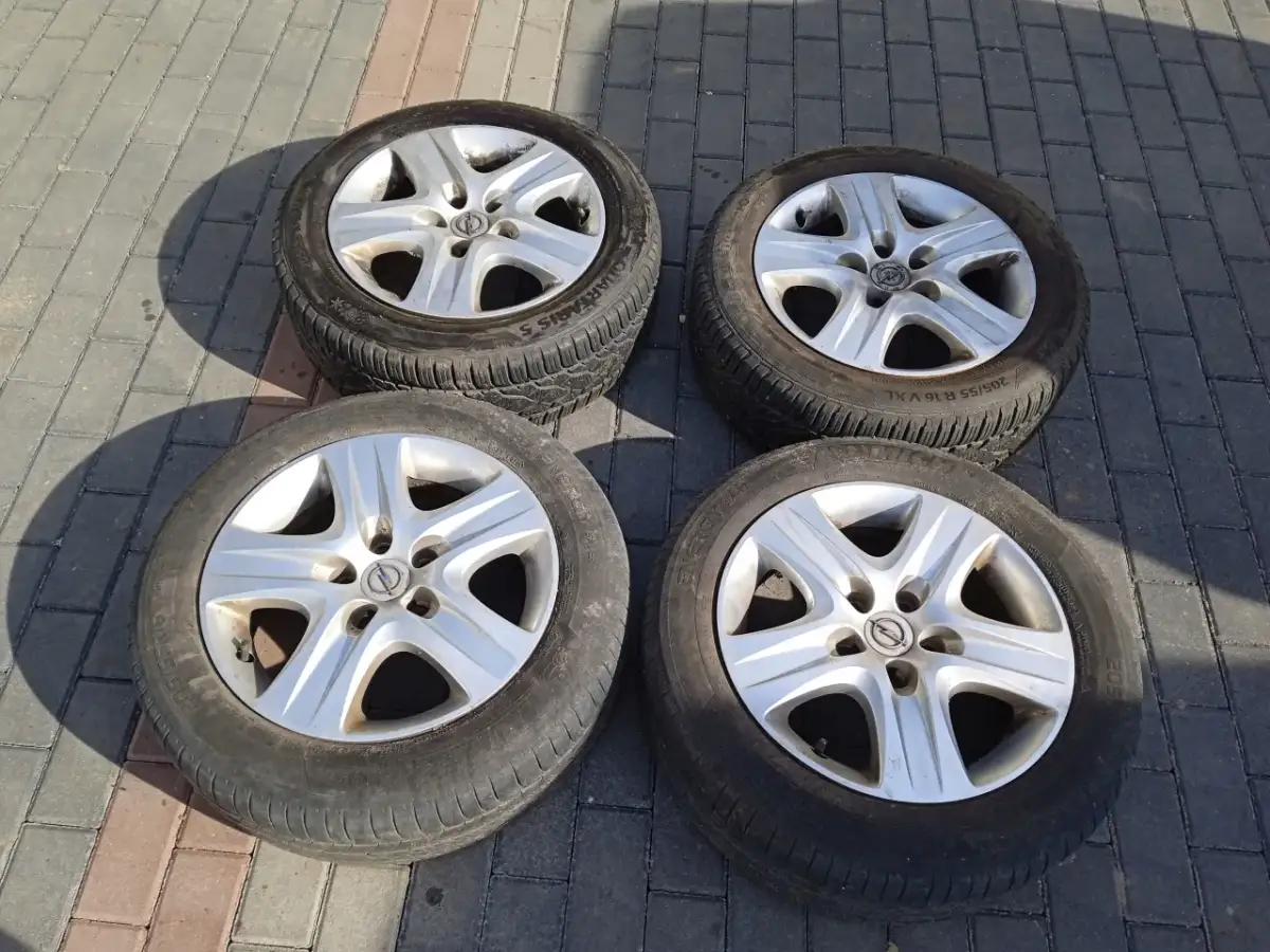 Cztery felgi strukturalne Opel z oponami leżą na chodniku.