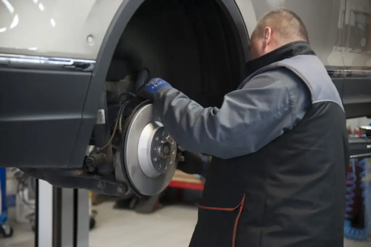 Mechanik sprawdza żywotność klocków hamulcowych przy tarczy hamulcowej samochodu na podnośniku.