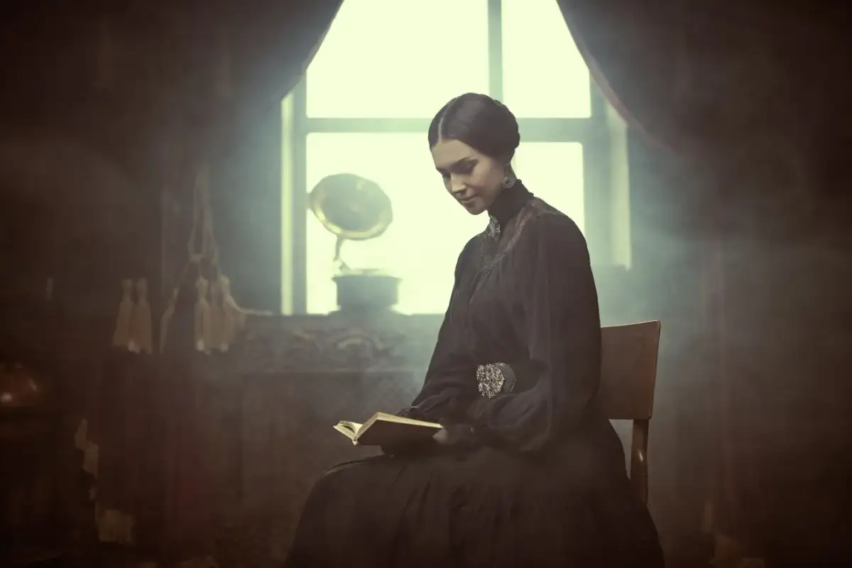 Młoda kobieta w czarnej sukni, przypominająca imię pani Bovary, czyta książkę przy oknie. W tle gramofon.