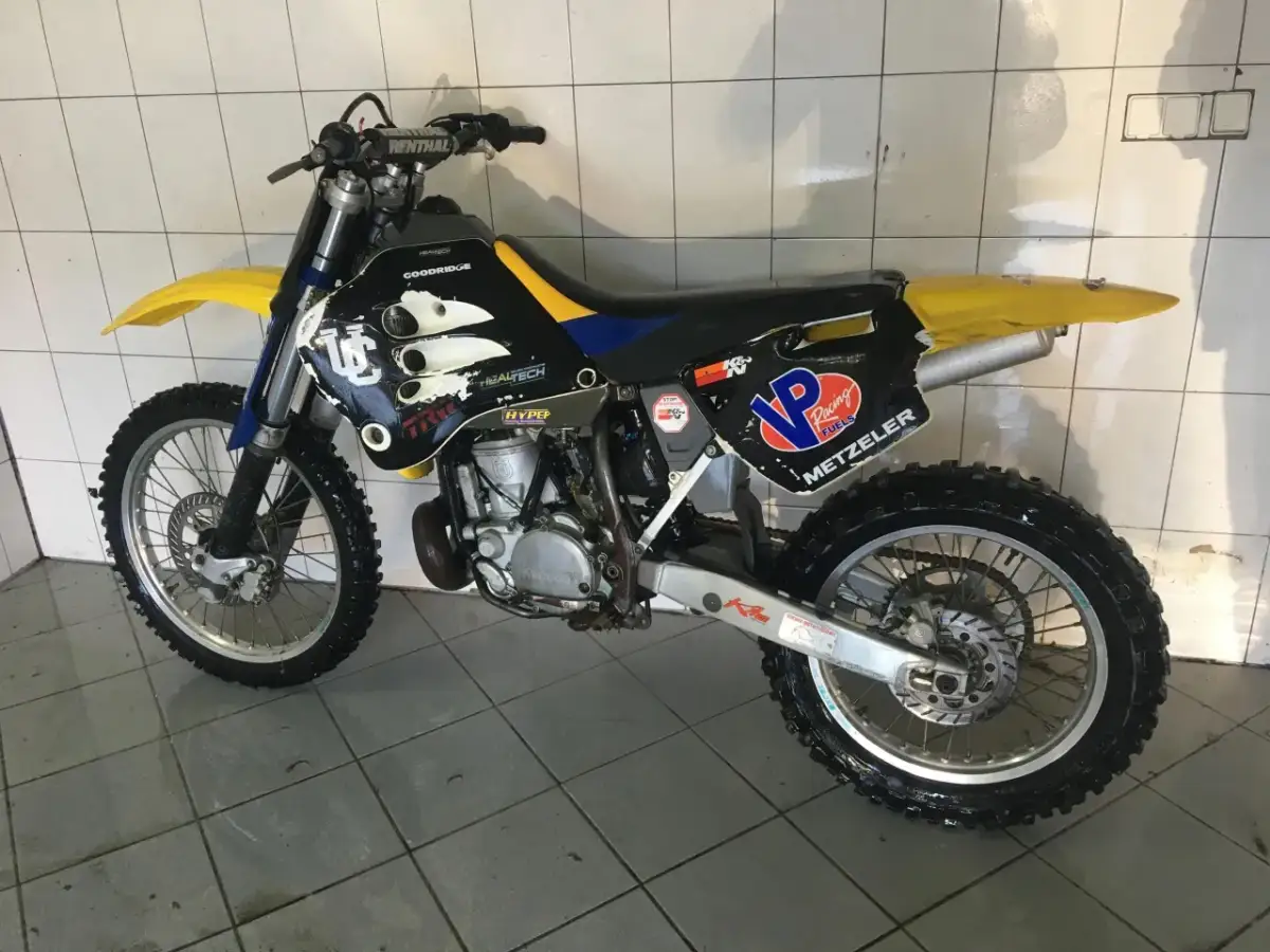 Husqvarna WR 250, gotowy do akcji. Czarne plastiki z żółtymi i niebieskimi akcentami, opony Metzeler.