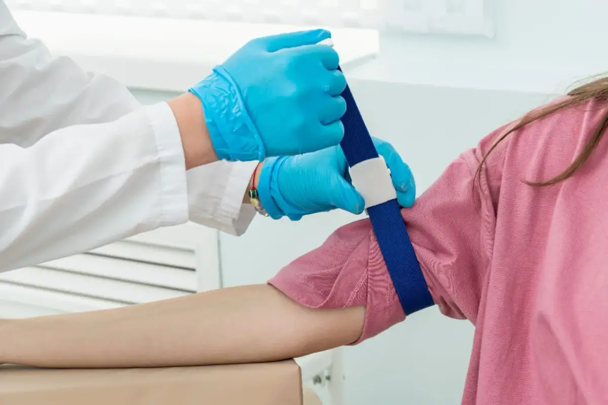 Pobieranie krwi u dziecka z podwyższonymi limfocytami. Ręka dziecka z opaską uciskową, pielęgniarka w rękawiczkach przygotowuje się do wkłucia.