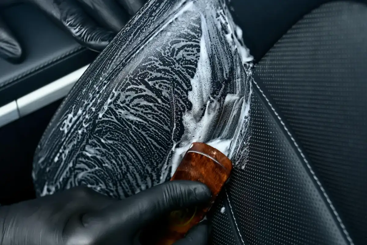 Rękawiczka w ręku aplikuje pianę na skórzane siedzenie samochodu. Pytanie: czym natłuścić skórę w samochodzie?