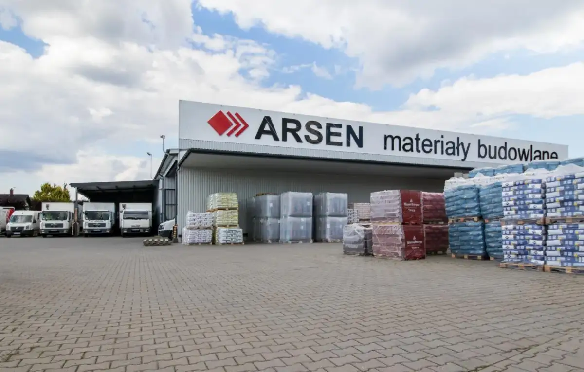 Budynek ARSEN materiały budowlane. Przed magazynem stoją ciężarówki i palety z materiałami. Sprawdź godziny otwarcia!