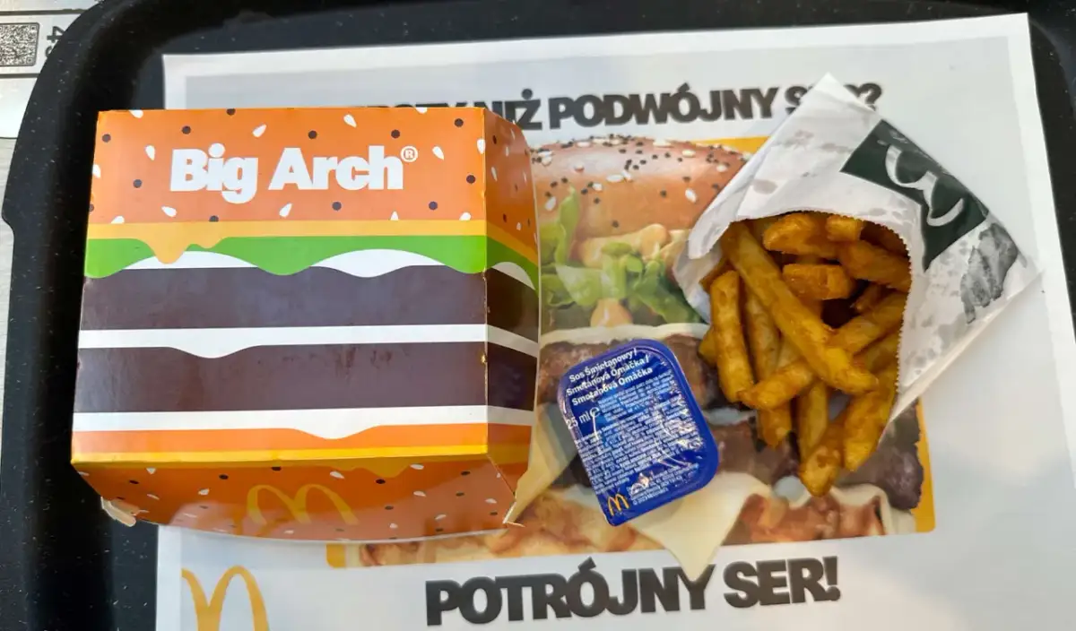 Duże frytki McDonald's w papierowym opakowaniu obok pudełka Big Arch i sosu.