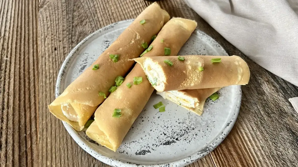 Rolowane naleśniki keto z mąki migdałowej, nadziewane kremowym farszem i posypane szczypiorkiem, prezentują się apetycznie na talerzu.