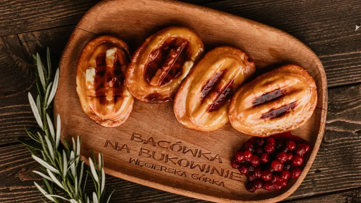 Cztery grillowane oscypki z żurawiną i rozmarynem na drewnianej desce.