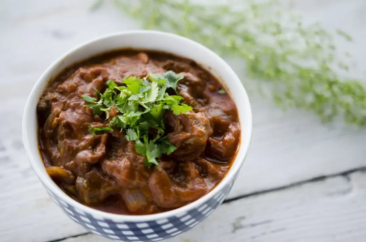 Miseczka z gęstym, pomarańczowym gulaszem tikka masala, ozdobiona świeżą kolendrą.
