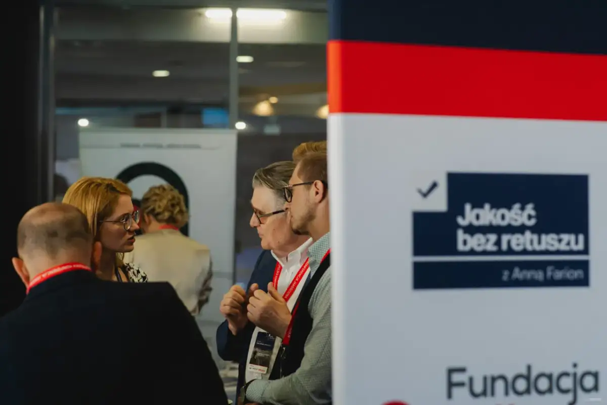 Ludzie rozmawiający na tle banera z napisem "Jakość bez retuszu".