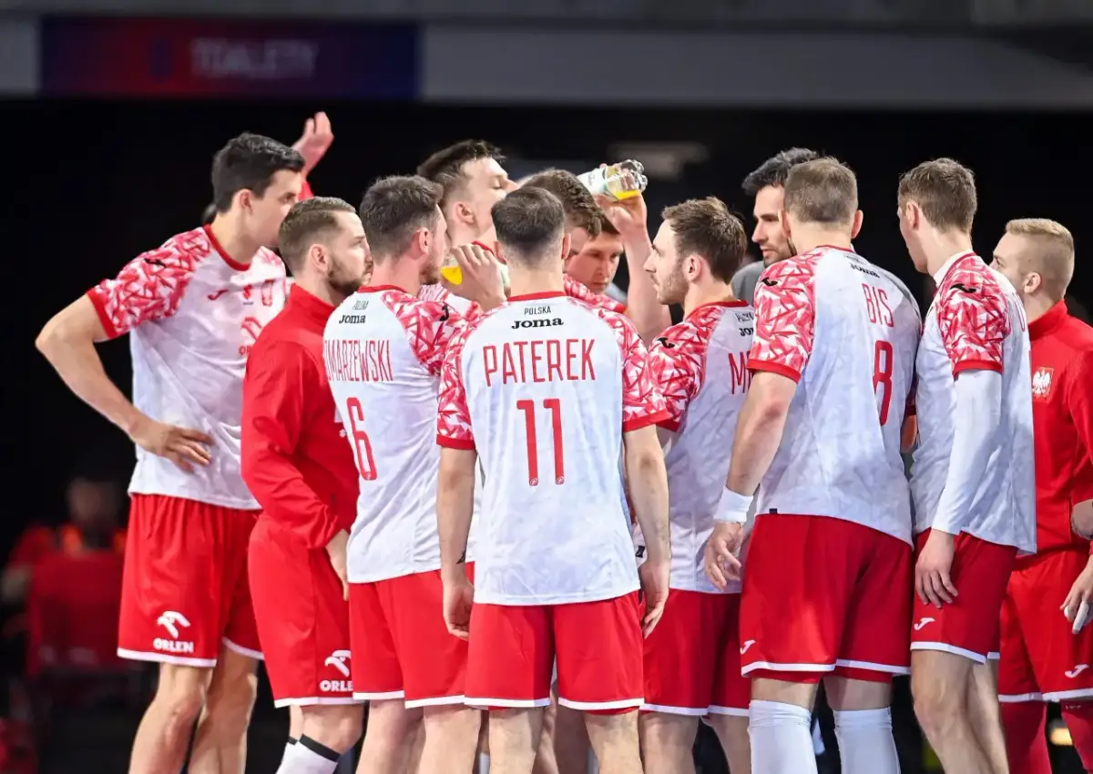 Drużyna piłkarzy ręcznych Polski w czerwono-białych strojach w skupieniu słucha trenera.