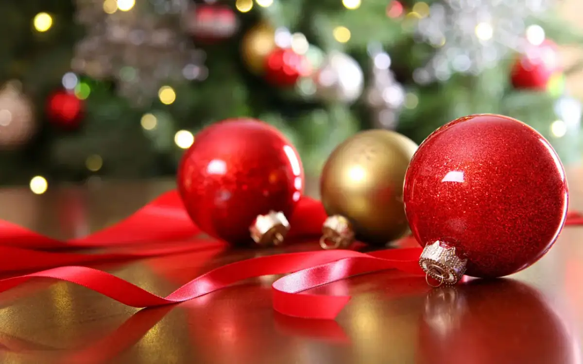 Czerwone i złote bombki, wstążka, choinka w tle. Czas, kiedy zdejmuje się ozdoby świąteczne, zbliża się nieubłaganie.
