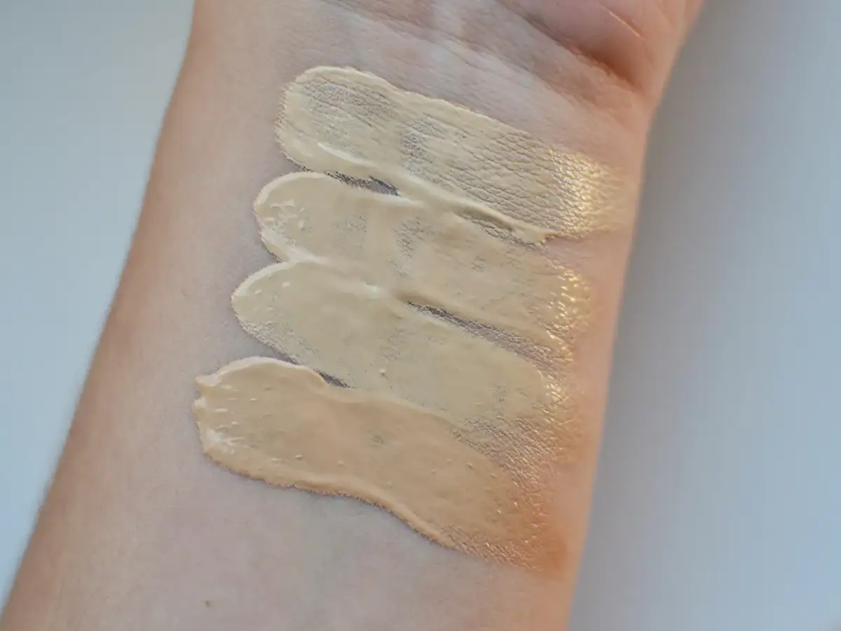 Smugi podkładu Eveline rozświetlającego na skórze. Testowanie odcieni dla idealnego dopasowania.