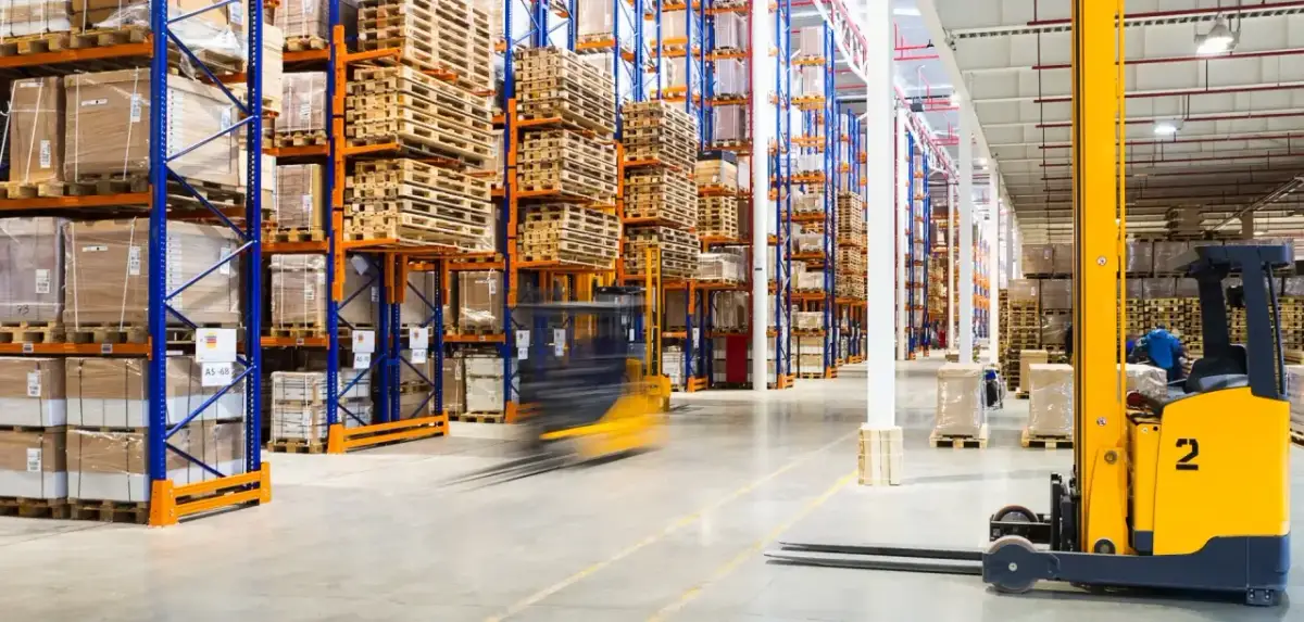 Wózek widłowy w ruchu w magazynie z wysokimi regałami pełnymi towarów i palet.