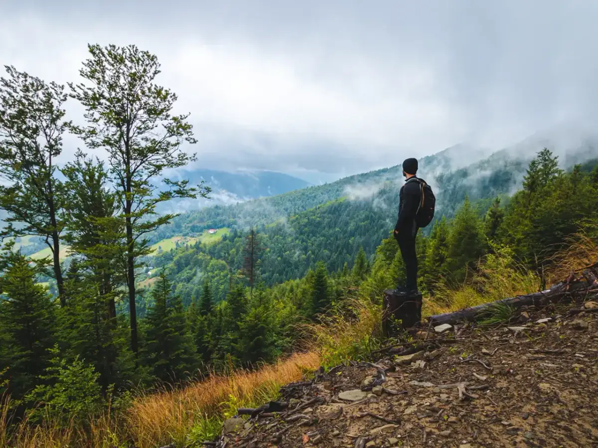Mężczyzna z plecakiem podziwia widok na górzyste, zalesione tereny. To prawdziwy hiking po polsku, z mgłą unoszącą się nad dolinami.