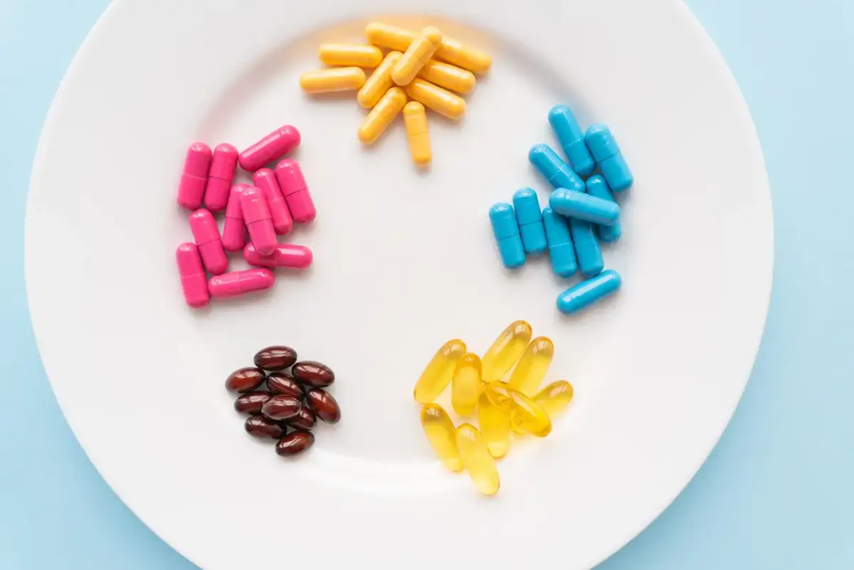Na białym talerzu ułożono kolorowe kapsułki: różowe, żółte, niebieskie oraz brązowe i żółte żelowe. Zastanawiasz się, jakie suplementy warto brać?